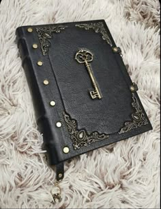 a black leather book with a golden key on it sitting on a fluffy white blanket