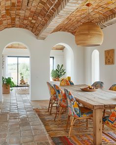 a dining room table with colorful chairs and an archway leading to the living room area