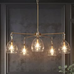 a chandelier with five lights hanging from it's sides, in front of a gray wall