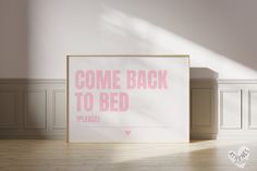 a pink poster with the words come back to bed on it in front of a white wall