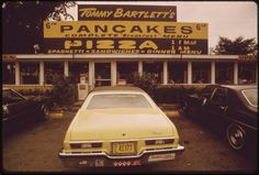 an old yellow car parked in front of a pancake's pizzeria