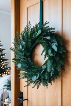 a wreath hanging on the front door of a house with christmas trees in the background