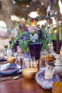 a wooden table topped with lots of purple and white flowers next to glasses filled with liquid