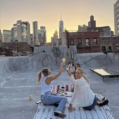 two women sitting on top of a skateboard ramp holding wine glasses in the air