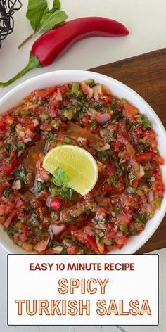 a white bowl filled with lots of food on top of a wooden table next to a red pepper