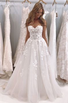 a woman is standing in front of dresses on display at a bridal shop,