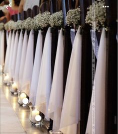 rows of candles are lined up along the side of a wall with white flowers on them