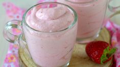 two glasses filled with strawberry pudding on top of a wooden board