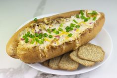 a hot dog on a bun with cheese and green onions next to crackers in a white plate