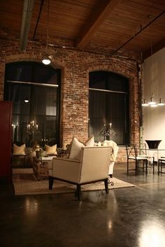 a living room filled with furniture next to two large windows in front of a brick wall