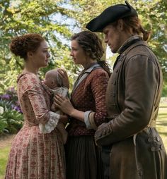 three people dressed in period clothing stand together and look at each other while holding a baby