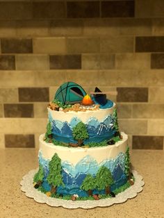 a three tiered cake is decorated with mountains and trees, camping items, and a tent