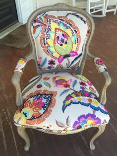 an old chair with colorful fabric on it's back and arm rests on a wood floor