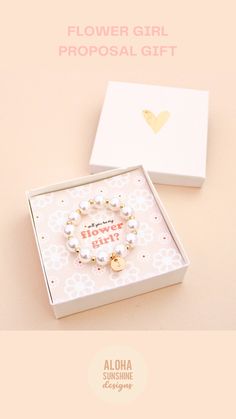 the flower girl gift box is open and has a white bracelet with gold charms on it