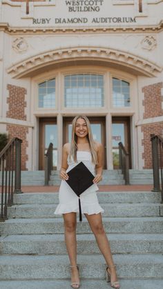 a woman standing on steps in front of a building holding a black and white book