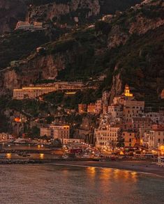 the city lights are lit up on the hillside above the water's edge as it reflects off in the ocean