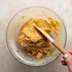 a hand holding a wooden spoon in a bowl filled with batter and orange powdered sugar