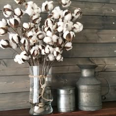 a vase filled with cotton sitting on top of a wooden shelf next to two metal containers