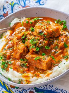 a bowl filled with meat and gravy on top of mashed potatoes