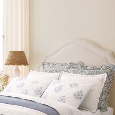 a white bed topped with pillows and blankets next to a lamp on top of a table