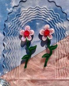 two pink flowers sitting on top of a piece of paper with wavy lines in the background