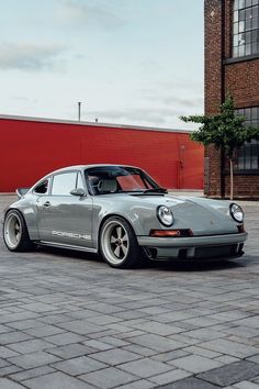 a grey porsche parked in front of a red brick building on a cobblestone street