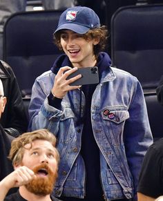 a man in a denim jacket and cap is taking a selfie with his cell phone