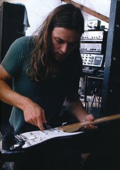 a man with long hair playing an electric guitar in a room full of sound equipment