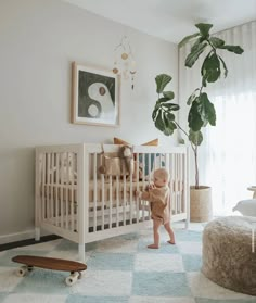 a baby standing next to a white crib in a room with blue and green rugs