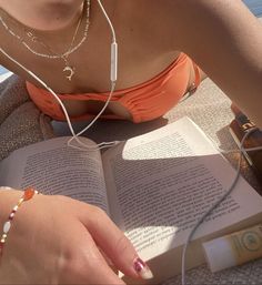 a woman sitting on the ground reading a book and listening to headphones with her hands