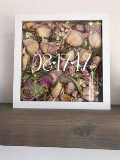 a white frame with flowers and the number 11 on it is sitting on top of a wooden shelf