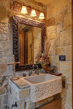 a bathroom sink sitting under a mirror next to a wooden cabinet and light fixture on a stone wall