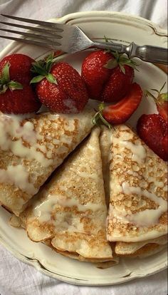 some pancakes with strawberries on a plate next to a fork and knife, ready to be eaten