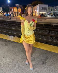 a woman in a yellow dress is standing on the train tracks and posing for a photo