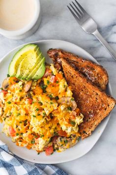 scrambled eggs, toast and avocado on a plate next to a cup of coffee