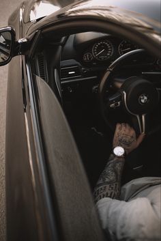 a man sitting in the driver's seat of a car with his hand on the steering wheel