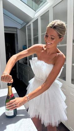 a woman in a white dress pouring champagne into a glass bottle on top of a counter