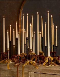 a bunch of candles that are on top of a mantle with ribbons around them and bows