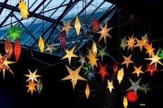 many colorful stars hanging from the ceiling in a room with glass walls and metal beams