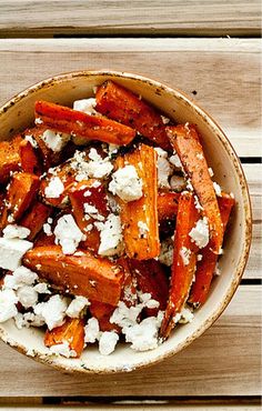 a bowl filled with carrots and feta cheese on top of a wooden table