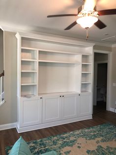 a living room with white bookcases and ceiling fan