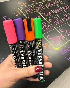 three crayons are held in front of a chalkboard with writing on it