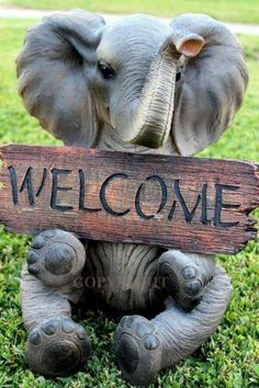 an elephant holding a welcome sign in its trunk on the grass with it's trunk up