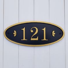 a black and gold house number sign on a white wooden wall with the number twelve eleven