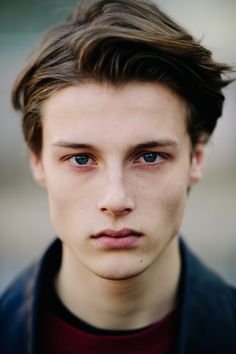 a close up of a person wearing a black shirt and blue eyes with a serious look on his face