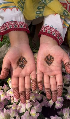 two hands with henna tattoos on them and some flowers in the foregrounds