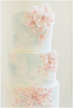 a three tiered wedding cake with pink flowers on the top and bottom, in pastel colors