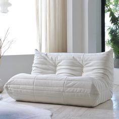 a white couch sitting on top of a hard wood floor next to a vase filled with flowers