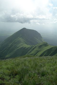 a grassy field on top of a mountain under a cloudy sky with mountains in the background