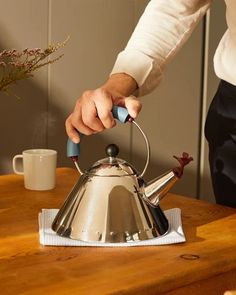 a person holding a tea kettle on top of a wooden table